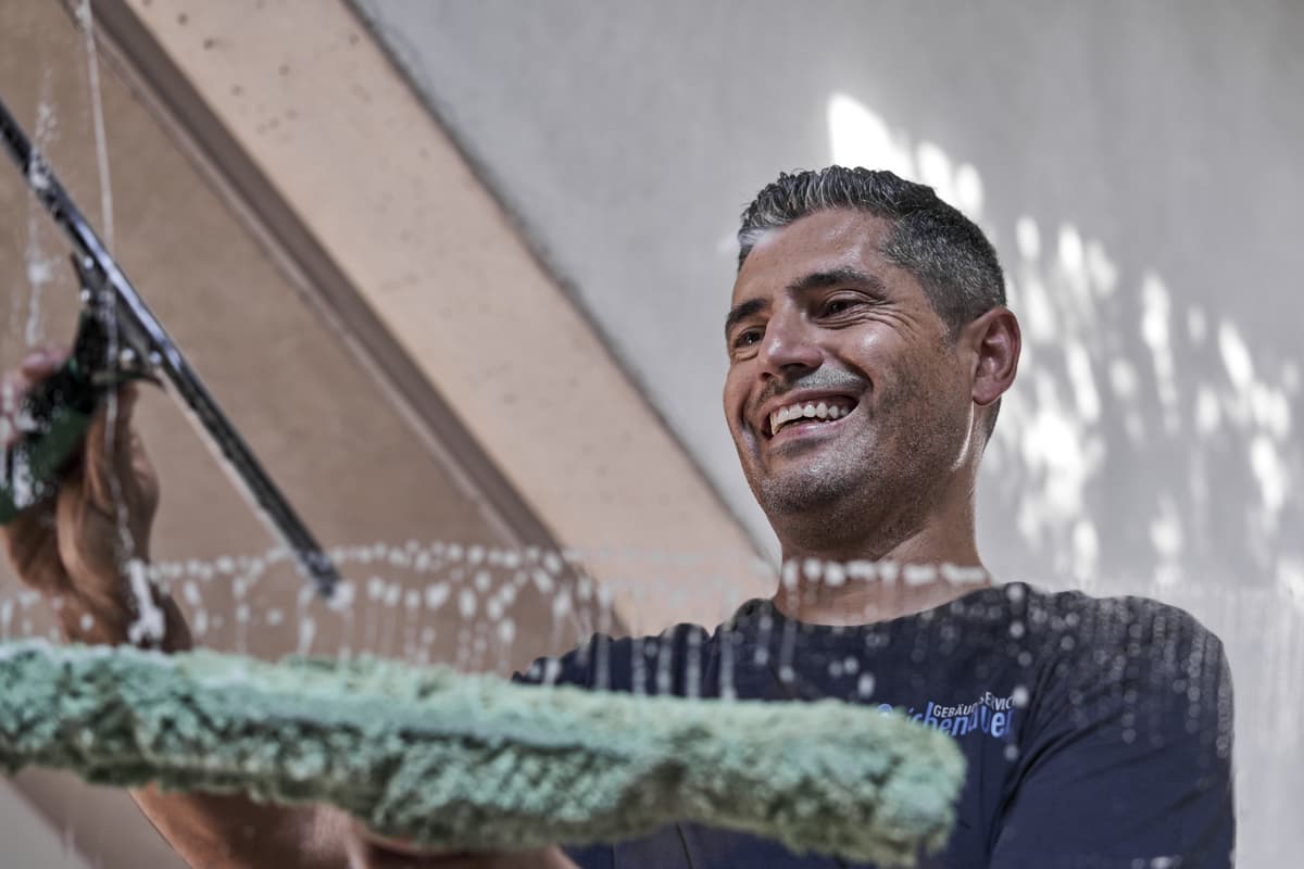 Mitarbeiter bei der Fensterreinigung, lächelt und nutzt einen Abzieher.