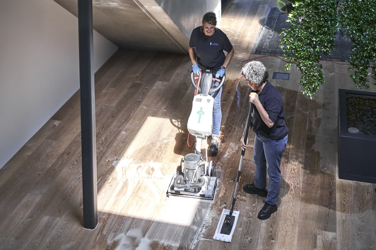 Zwei Reinigungskräfte bei der Bodenpflege mit Maschinen in einem modernen Gebäude.