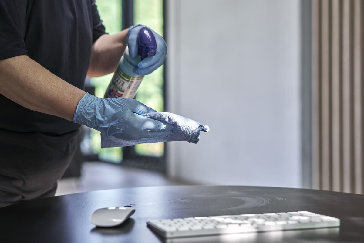 Reinigung einer Tischoberfläche mit Handschuhen und Desinfektionsmittel.